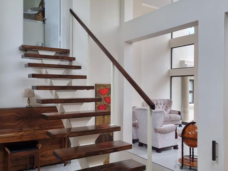 A bright and spacious entrance hall featuring a modern floating staircase with wooden treads and a double volume ceiling, leading into an open living area.