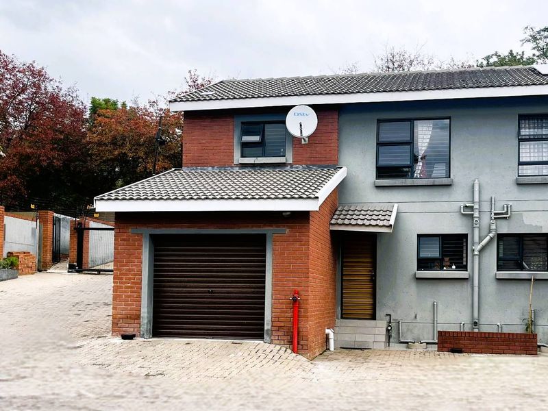 Front elevation of a two-story townhouse featuring a single garage, brick and plaster facade, tiled roof, and paved driveway area.