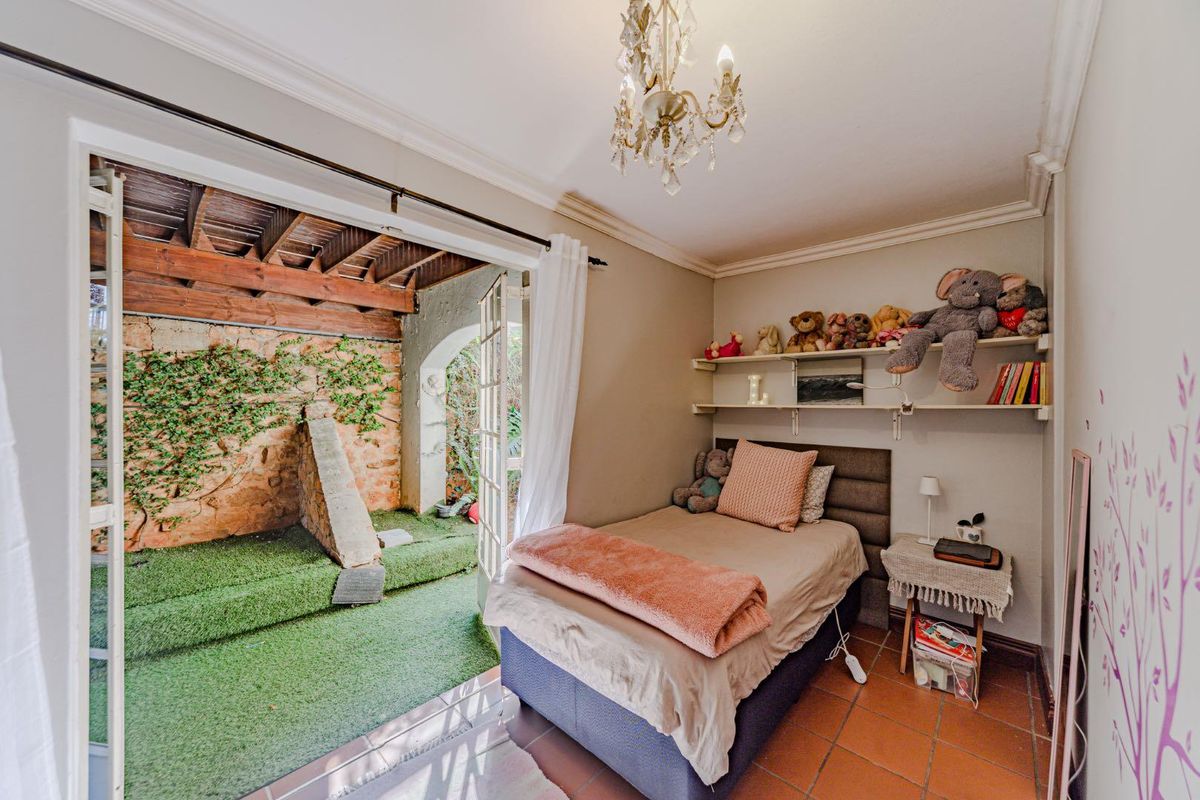 A cozy bedroom featuring terracotta flooring, crown molding, and direct access through French doors to a private outdoor patio area with stone wall features.