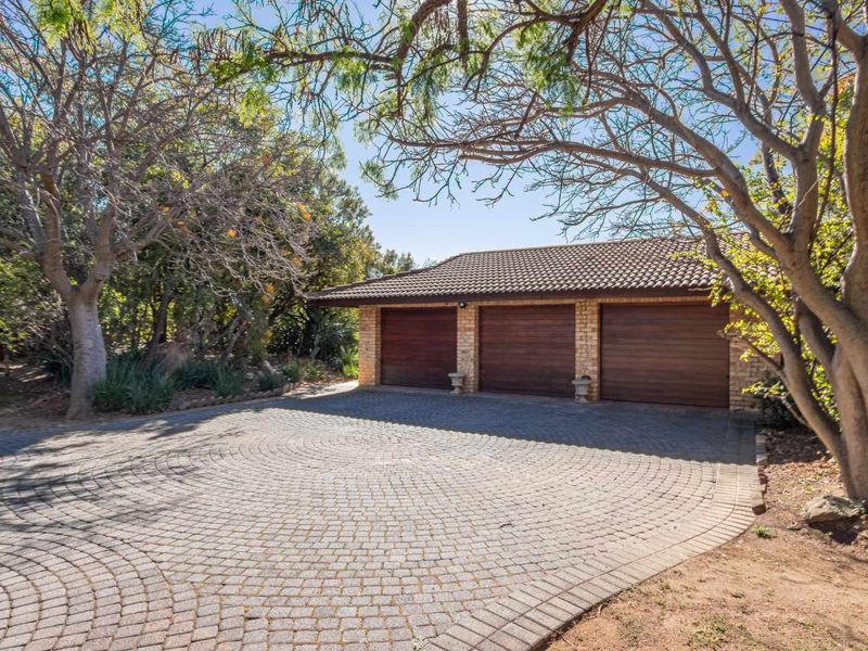 A well-maintained triple garage with a brick-paved driveway, set within a mature, tree-lined garden environment.
