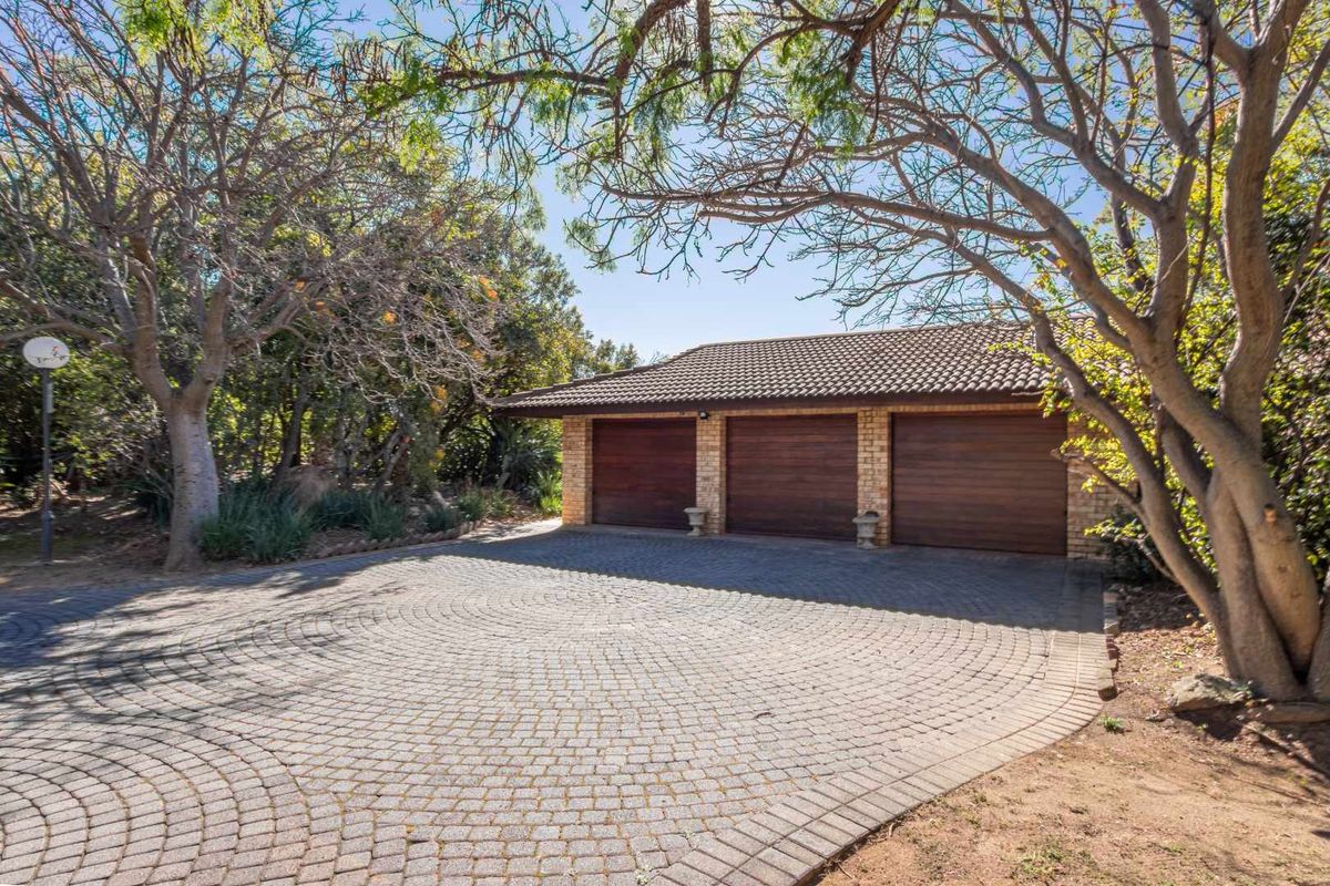 A well-maintained triple garage with a brick-paved driveway, set within a mature, tree-lined garden environment.