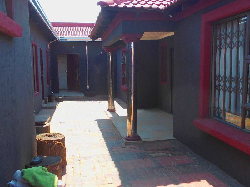 A paved rear courtyard area featuring dark exterior walls with red trim, decorative metal pillars, and tiled roofing.