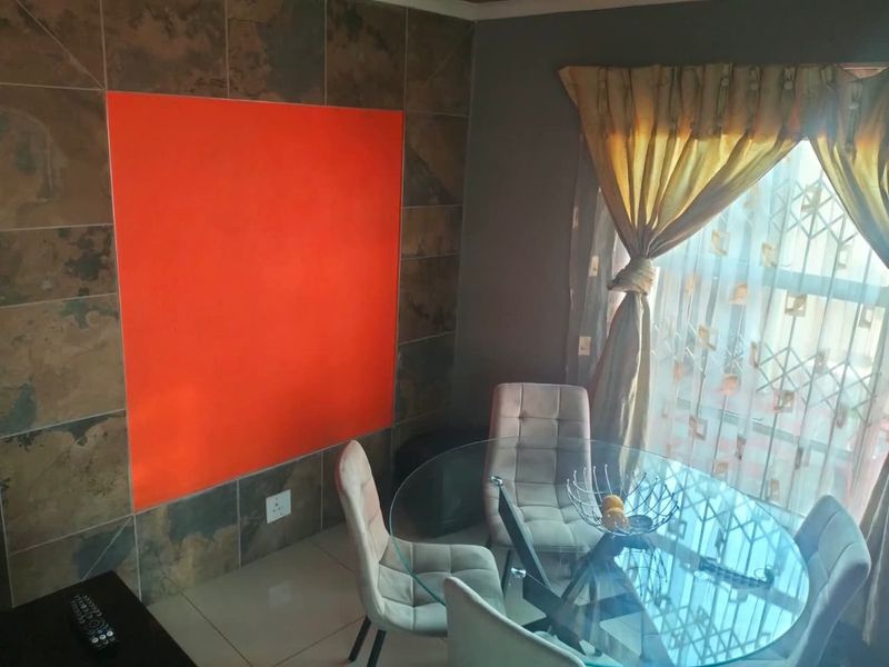 Dining area featuring a tiled accent wall and large window with security gate, providing a functional space for meals.
