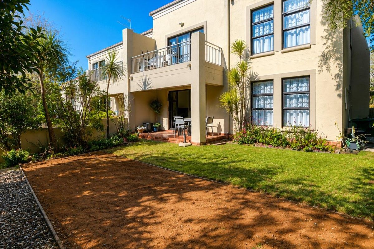 Rear view of the townhouse featuring a private garden, paved patio area, and an upper-level balcony with sliding door access.