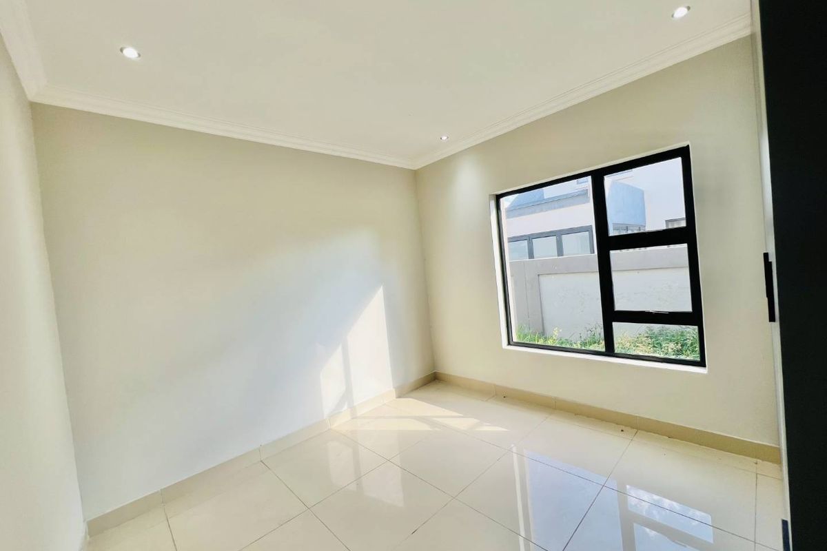 A bright, empty bedroom featuring neutral tiled flooring, recessed ceiling lighting, and a large window with a black frame.