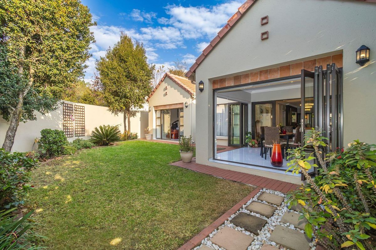 A well-maintained rear garden featuring a manicured lawn, brick pathways, and seamless indoor-outdoor flow through large bi-fold doors into the living area.