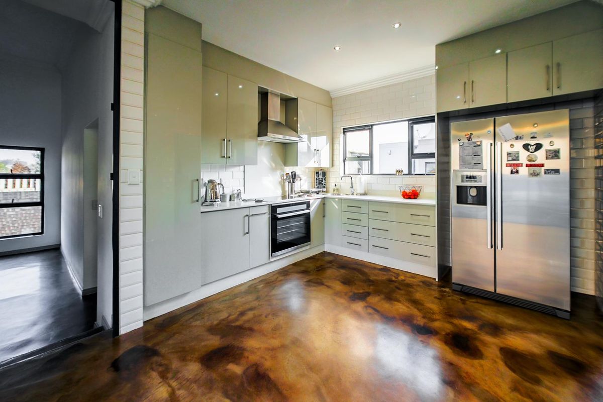 Modern kitchen featuring high-gloss cabinetry, subway tile backsplash, integrated oven, extractor fan, and unique polished epoxy resin flooring.