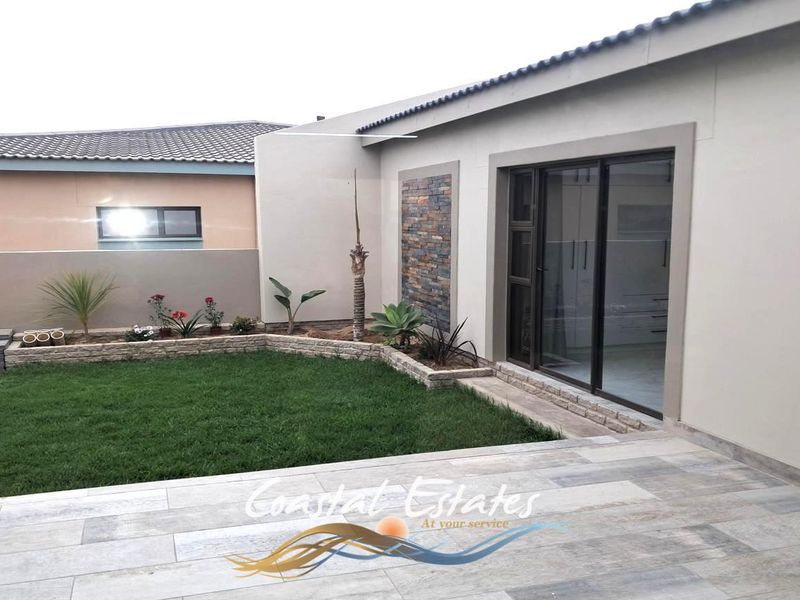 A well-maintained rear exterior featuring a tiled patio, a small lawn with a stone-clad retaining wall, and a modern sliding glass door entrance.