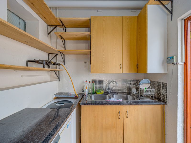 A functional scullery or utility area featuring double stainless steel sinks, laminate cabinetry, open shelving, and a mosaic tile splashback.
