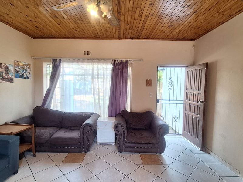 A living room featuring a timber tongue and groove ceiling, ceramic tiled flooring, and direct access to the exterior via a security gate.