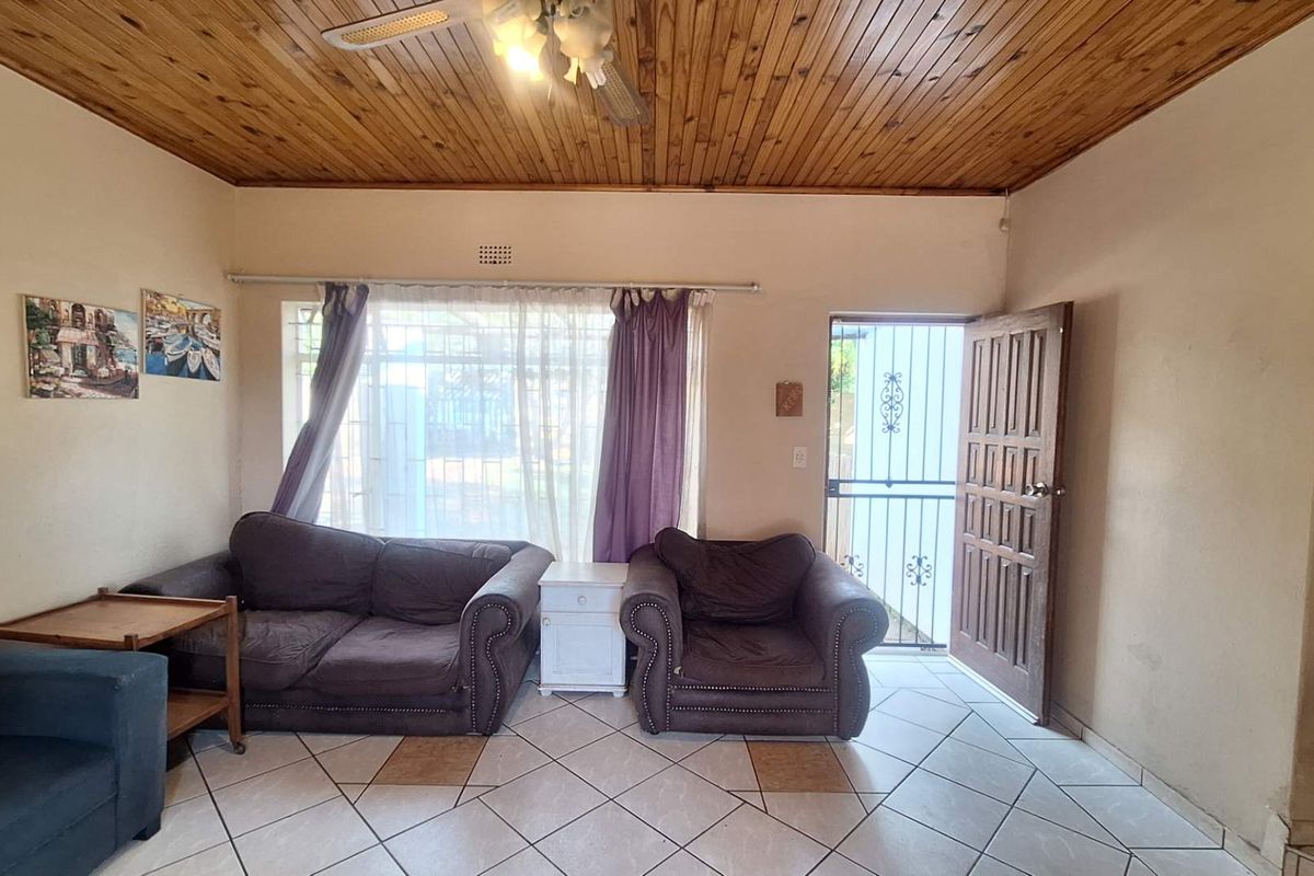 A living room featuring a timber tongue and groove ceiling, ceramic tiled flooring, and direct access to the exterior via a security gate.
