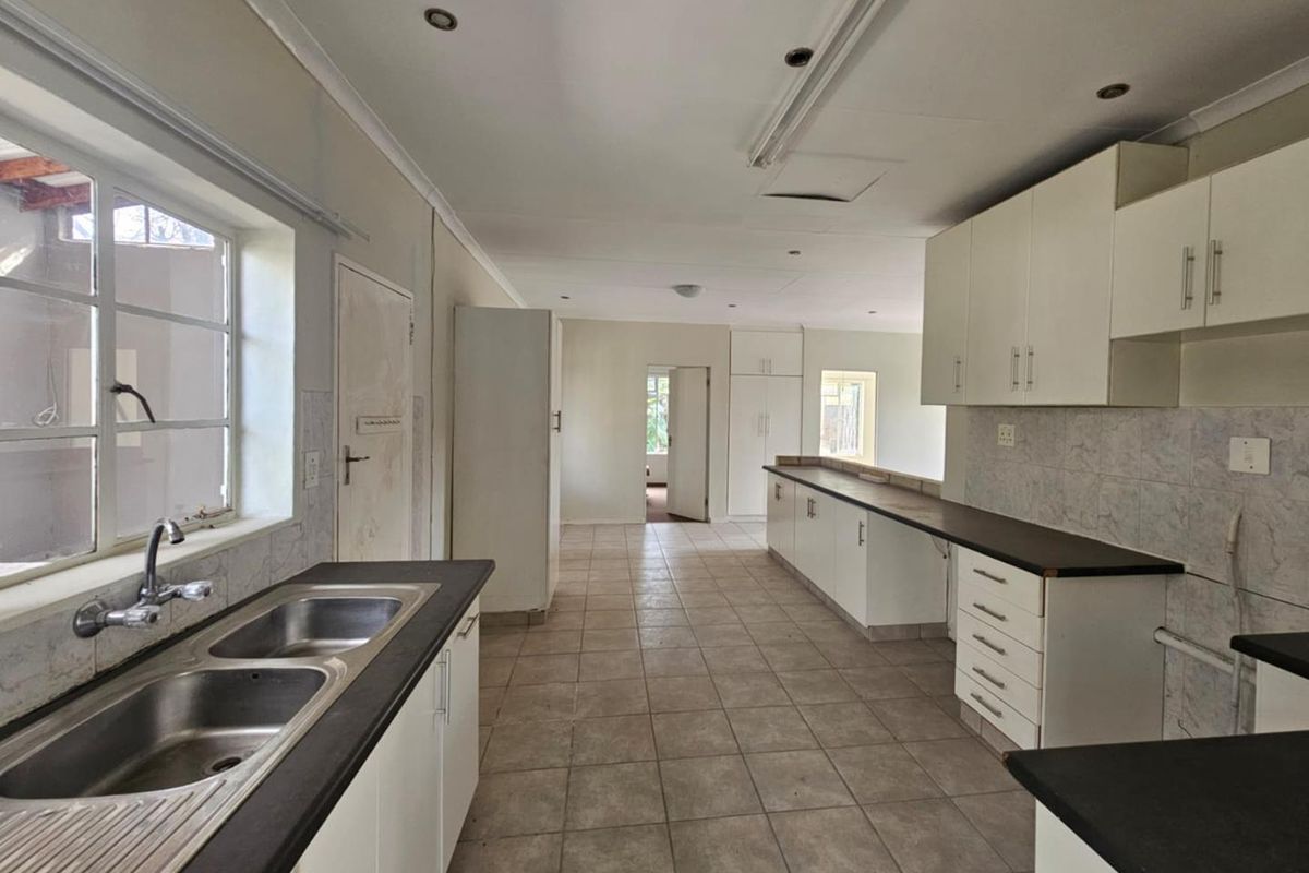 Spacious kitchen featuring extensive white cabinetry, dark countertops, double stainless steel sink, and tiled flooring, offering a functional layout with ample storage space.