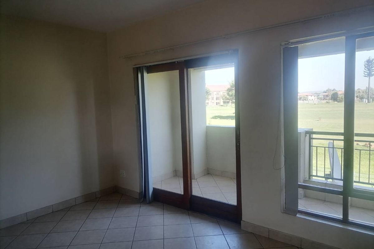 A bright, empty living area featuring tiled flooring and large sliding glass doors that open onto a private balcony with scenic views.