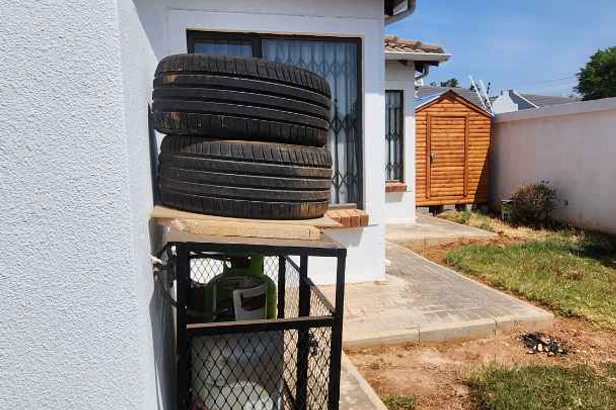 A view of the rear exterior featuring a paved walkway, a secure gas cylinder cage, and a small wooden garden shed.
