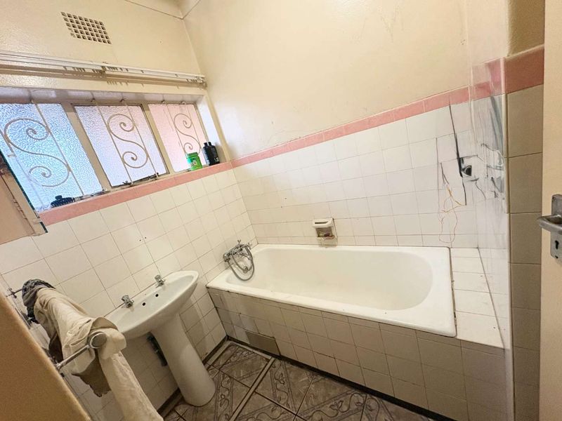 A dated bathroom featuring a pedestal basin and built-in bathtub, requiring renovation to address damaged tiling and exposed wiring.