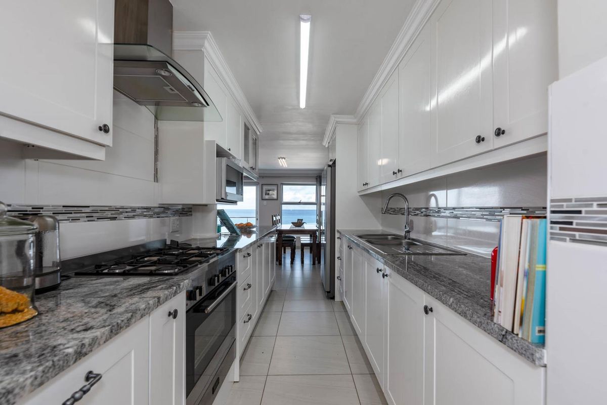 A galley-style kitchen featuring white cabinetry, granite countertops, a gas cooktop, stainless steel extractor fan, and a double basin sink.