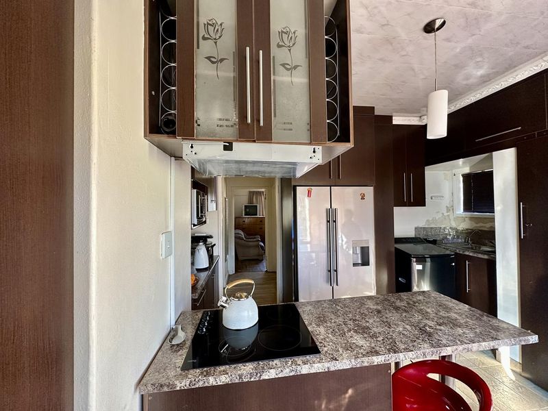A kitchen featuring dark cabinetry, laminate countertops, and an electric hob. The space shows signs of wear, particularly on the wall surfaces.