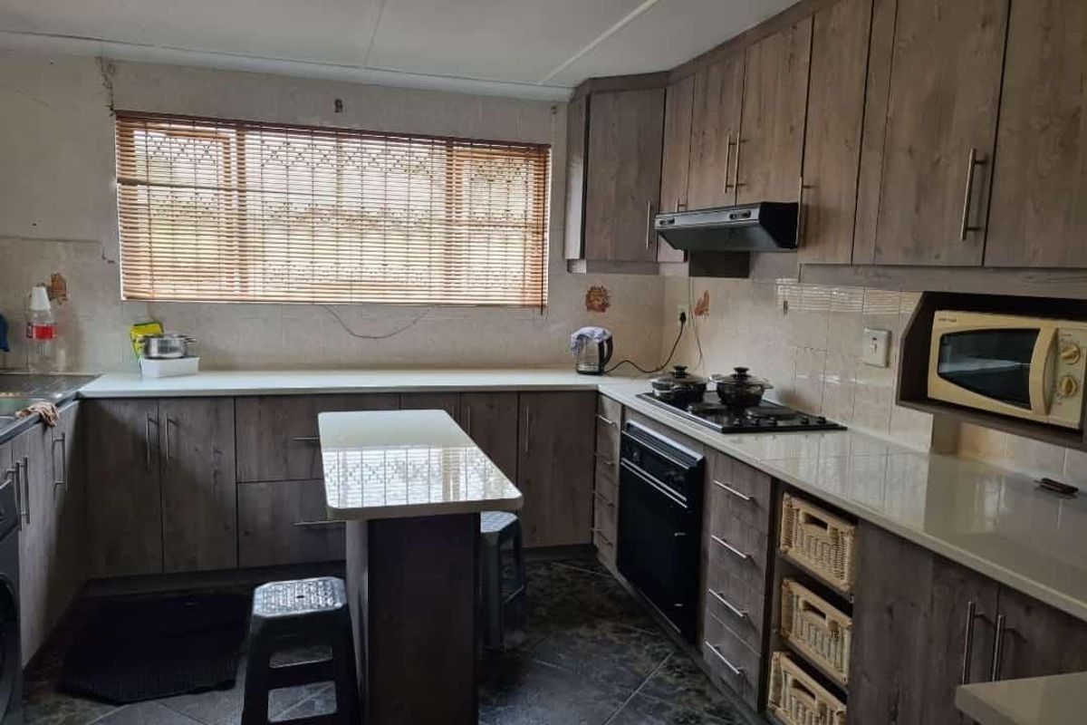 Functional kitchen featuring wood-look laminate cabinetry, stone countertops, built-in oven, gas hob, and integrated microwave with tiled flooring and backsplash.