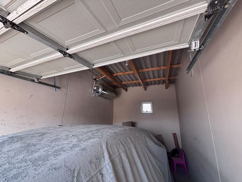 A functional garage space featuring a sectional door, exposed timber roof rafters, and a wall-mounted electric geyser.