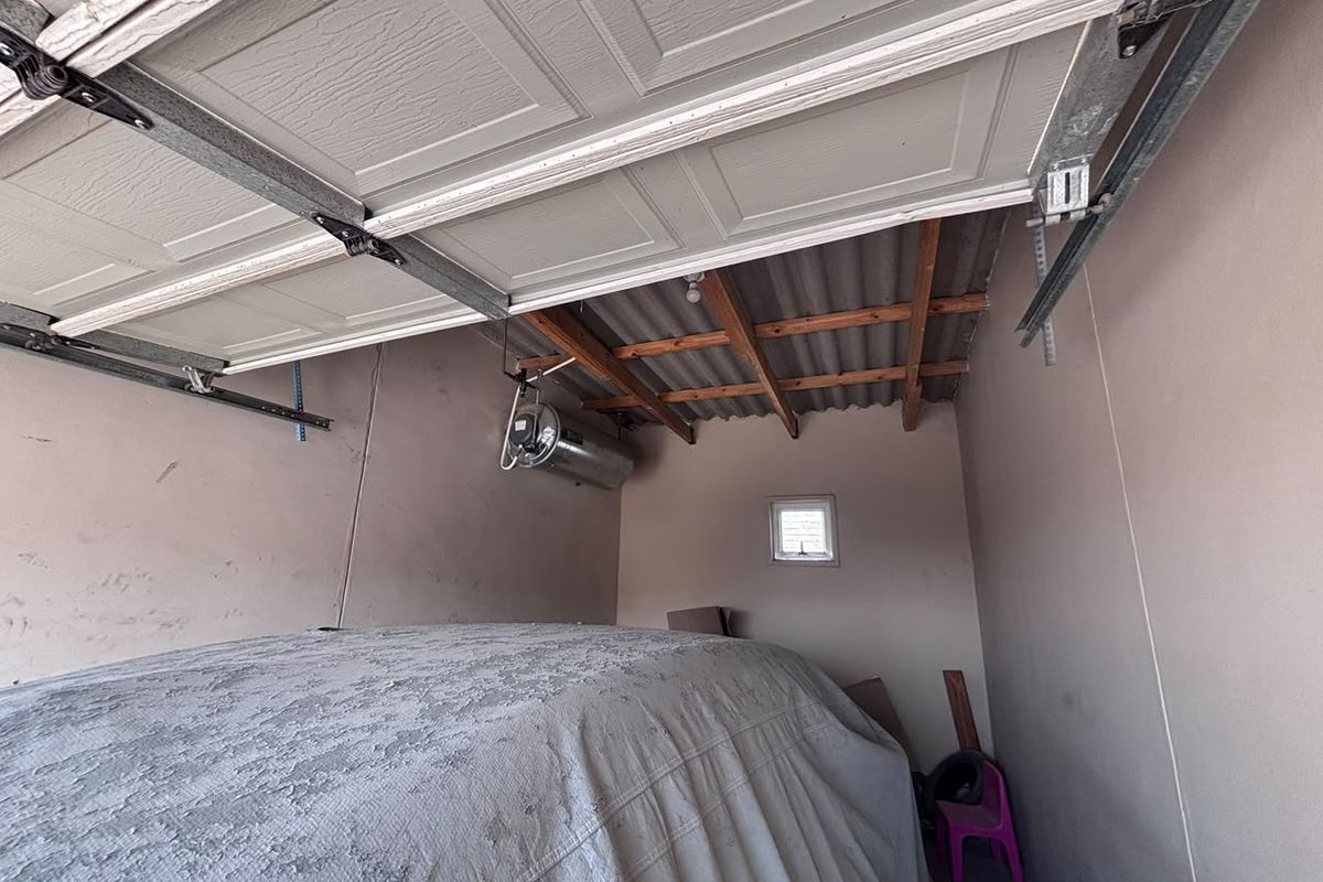A functional garage space featuring a sectional door, exposed timber roof rafters, and a wall-mounted electric geyser.