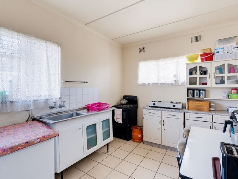 A functional kitchen featuring tiled flooring, built-in cabinetry, a stainless steel sink, and a freestanding stove, offering potential for modernization.