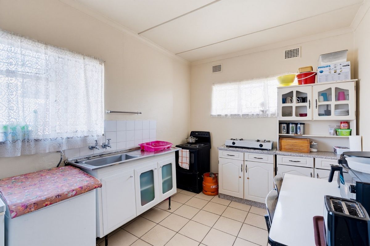 A functional kitchen featuring tiled flooring, built-in cabinetry, a stainless steel sink, and a freestanding stove, offering potential for modernization.