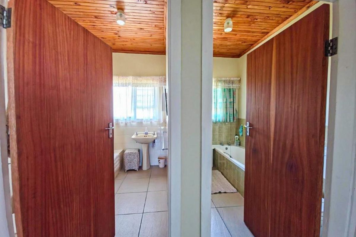 A view through two doorways into a bathroom featuring a pedestal basin, tiled flooring, and a built-in bathtub with a timber-paneled ceiling.