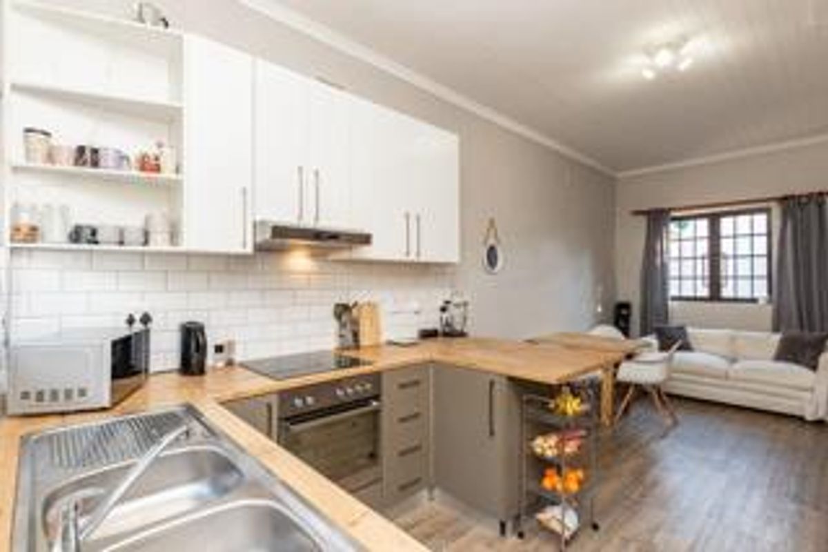 Modern open-plan kitchen featuring white and grey cabinetry, wooden countertops, subway tile backsplash, and integrated appliances, flowing into a comfortable living area.