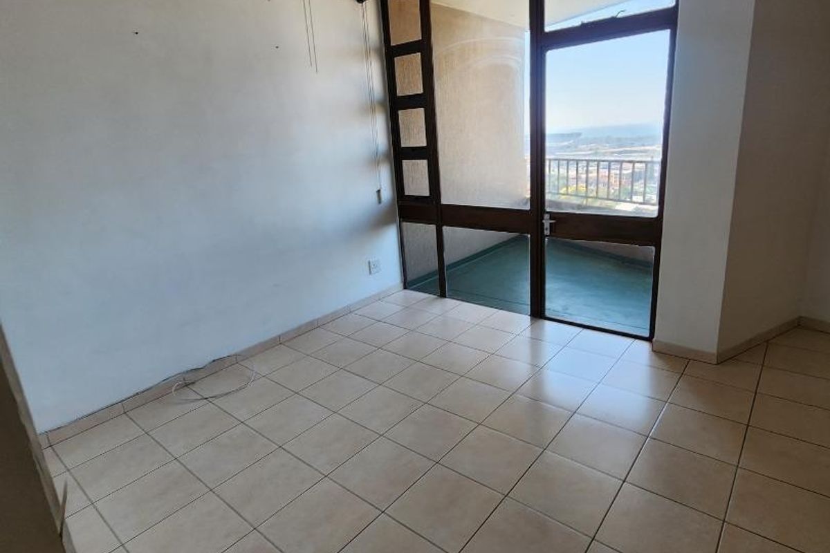 An empty living room featuring tiled flooring, a ceiling fan, and large glass doors providing access to a balcony with an outdoor view.