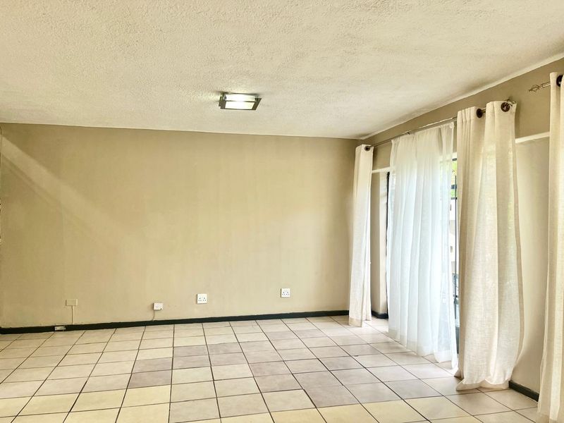 An empty living room featuring neutral wall paint, tiled flooring, and large windows with curtain tracks, offering a blank canvas for interior design.