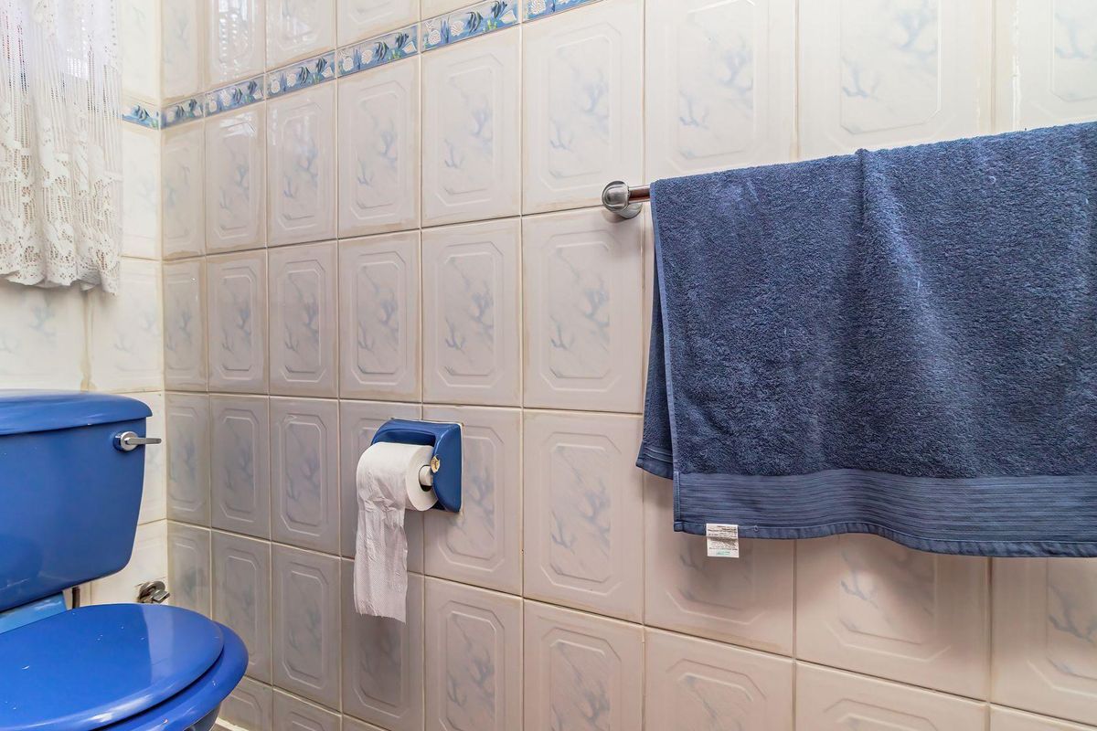 A dated bathroom featuring blue sanitaryware and patterned ceramic wall tiles, providing a functional space with potential for modern renovation.