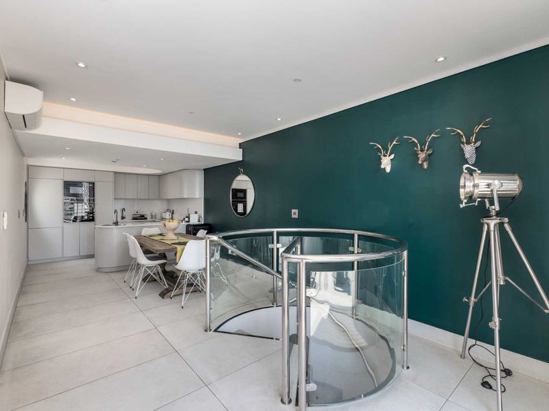 Modern open-plan living area featuring a striking spiral staircase with glass balustrade, sleek kitchen cabinetry, and contemporary tiled flooring.