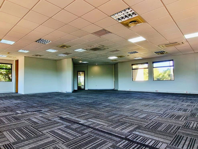 A spacious, open-plan office area featuring a suspended ceiling with recessed lighting, air conditioning, and durable carpet tiles, offering a versatile workspace.