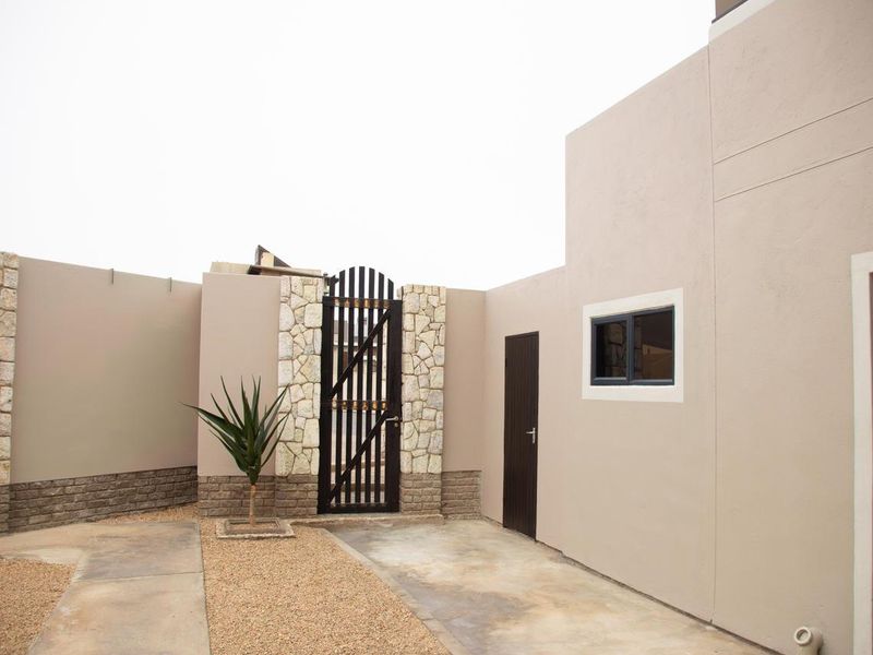A private rear courtyard area featuring stone-clad pillars, a secure metal gate, paved pathways, and gravel landscaping.