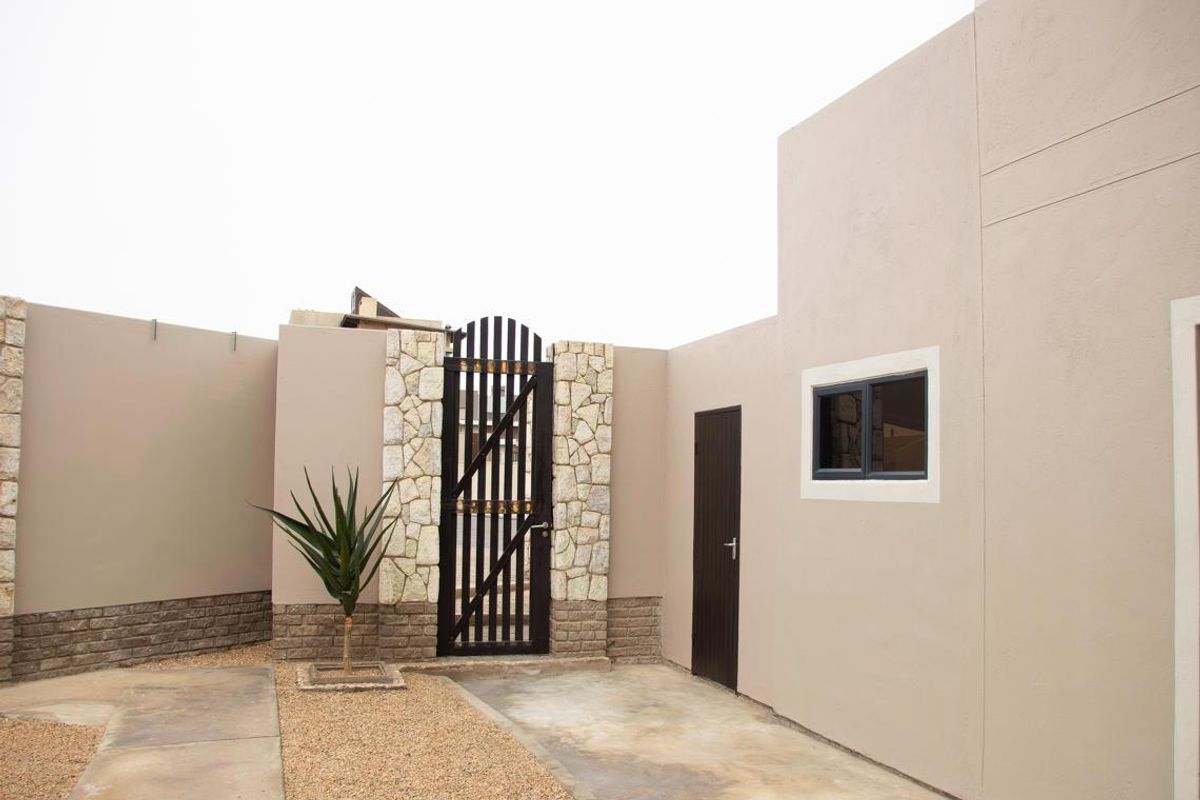A private rear courtyard area featuring stone-clad pillars, a secure metal gate, paved pathways, and gravel landscaping.