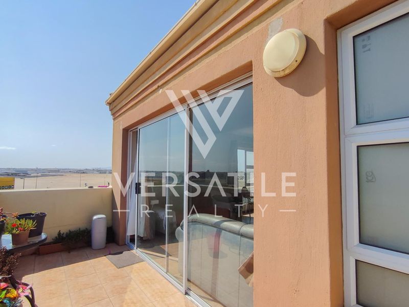 A tiled balcony area featuring a sliding glass door entrance, exterior wall lighting, and a parapet wall with views of the surrounding area.