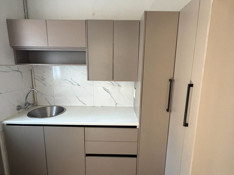 Compact kitchen area featuring modern taupe cabinetry, marble-look tile backsplash, and a stainless steel sink with tiled flooring.