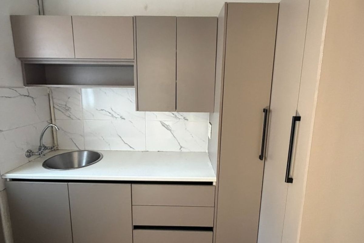 Compact kitchen area featuring modern taupe cabinetry, marble-look tile backsplash, and a stainless steel sink with tiled flooring.