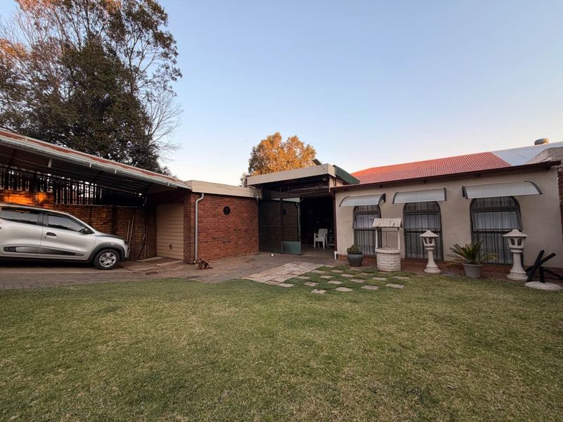 Rear exterior view of the property featuring a brick facade, attached garage, carport, and a well-maintained lawn area.