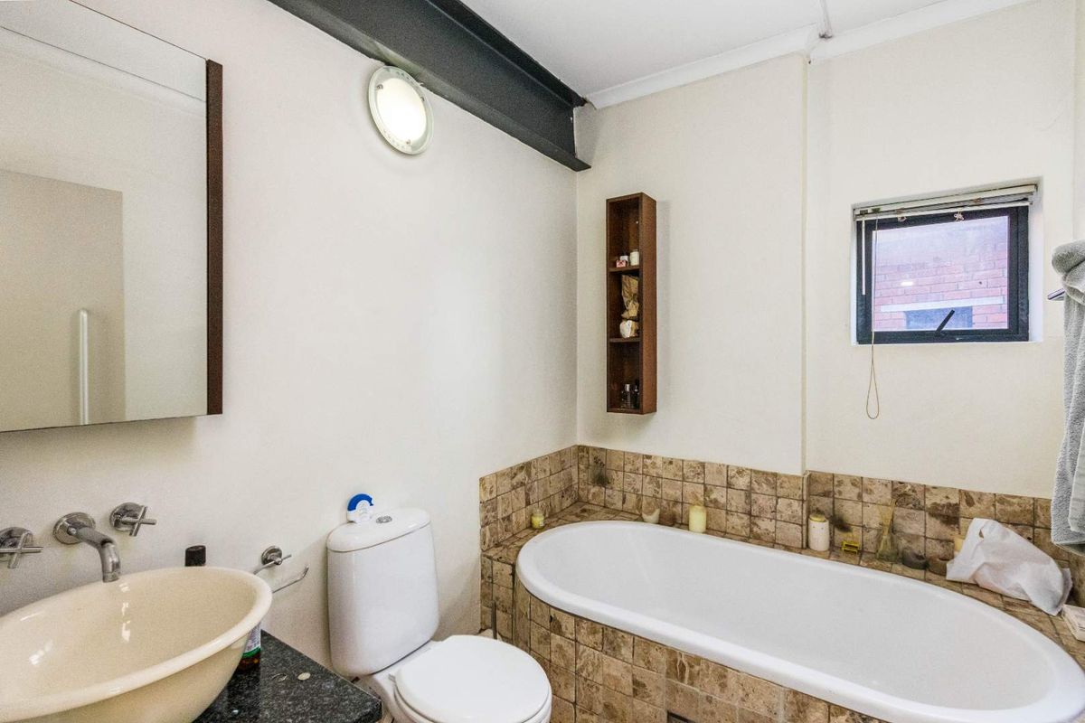 A functional bathroom featuring a built-in bathtub with tiled surround, a vessel sink vanity, and a wall-mounted toilet.