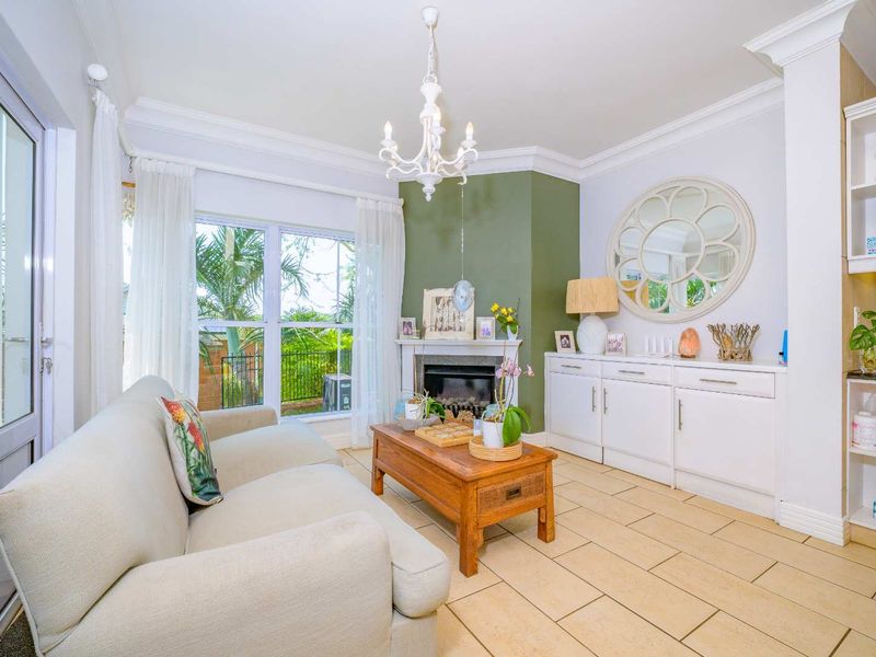 A bright living room featuring a fireplace, built-in cabinetry, tiled flooring, and crown molding, with direct access to the outdoor area.