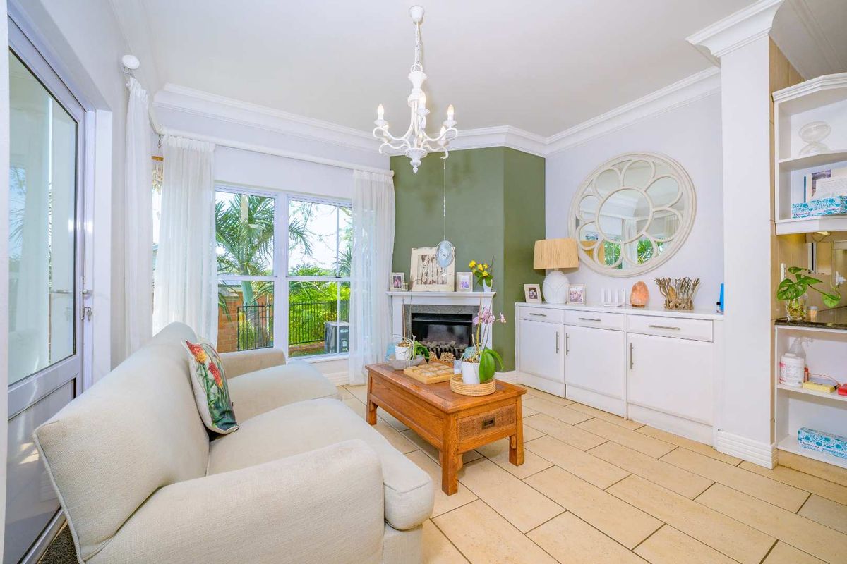 A bright living room featuring a fireplace, built-in cabinetry, tiled flooring, and crown molding, with direct access to the outdoor area.