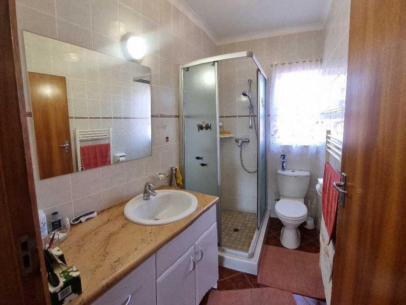 A functional bathroom featuring a vanity cabinet with a basin, a glass shower enclosure, and a toilet, finished with neutral wall tiles.