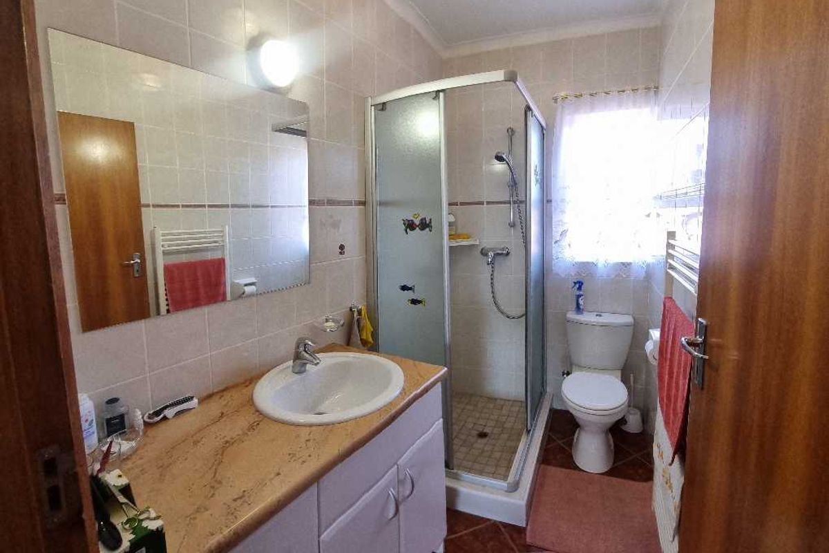 A functional bathroom featuring a vanity cabinet with a basin, a glass shower enclosure, and a toilet, finished with neutral wall tiles.