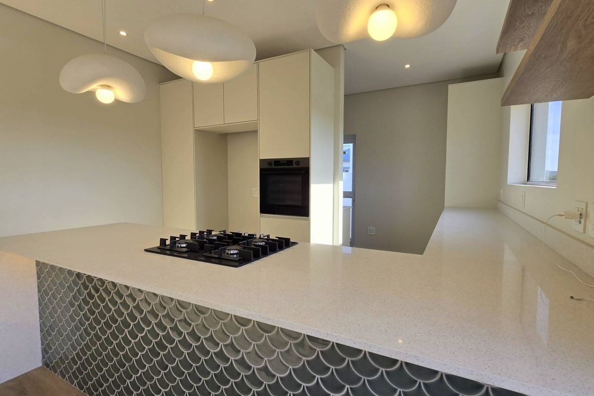 Modern kitchen featuring a large island with a gas hob, quartz countertops, and decorative scalloped tile detailing, complemented by contemporary pendant lighting.