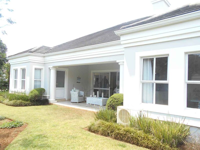 A well-maintained rear exterior view of the townhouse featuring a covered patio, landscaped garden, and sliding glass door access.