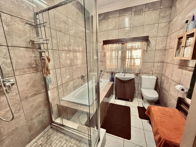 A functional bathroom featuring a glass shower enclosure, built-in bathtub, vanity basin, and toilet with neutral wall and floor tiling.