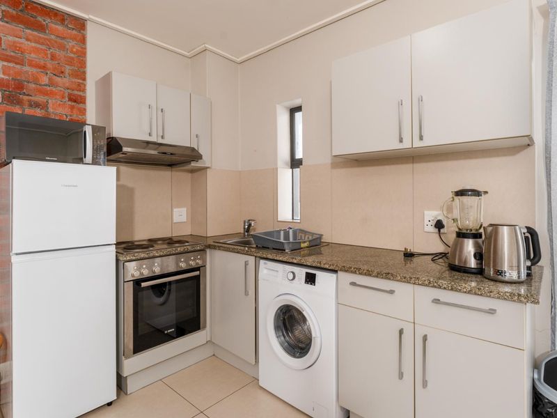 Compact kitchen featuring granite countertops, built-in oven, electric hob, extractor fan, and an exposed brick feature wall with tiled flooring.