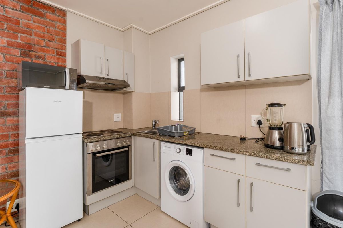Compact kitchen featuring granite countertops, built-in oven, electric hob, extractor fan, and an exposed brick feature wall with tiled flooring.