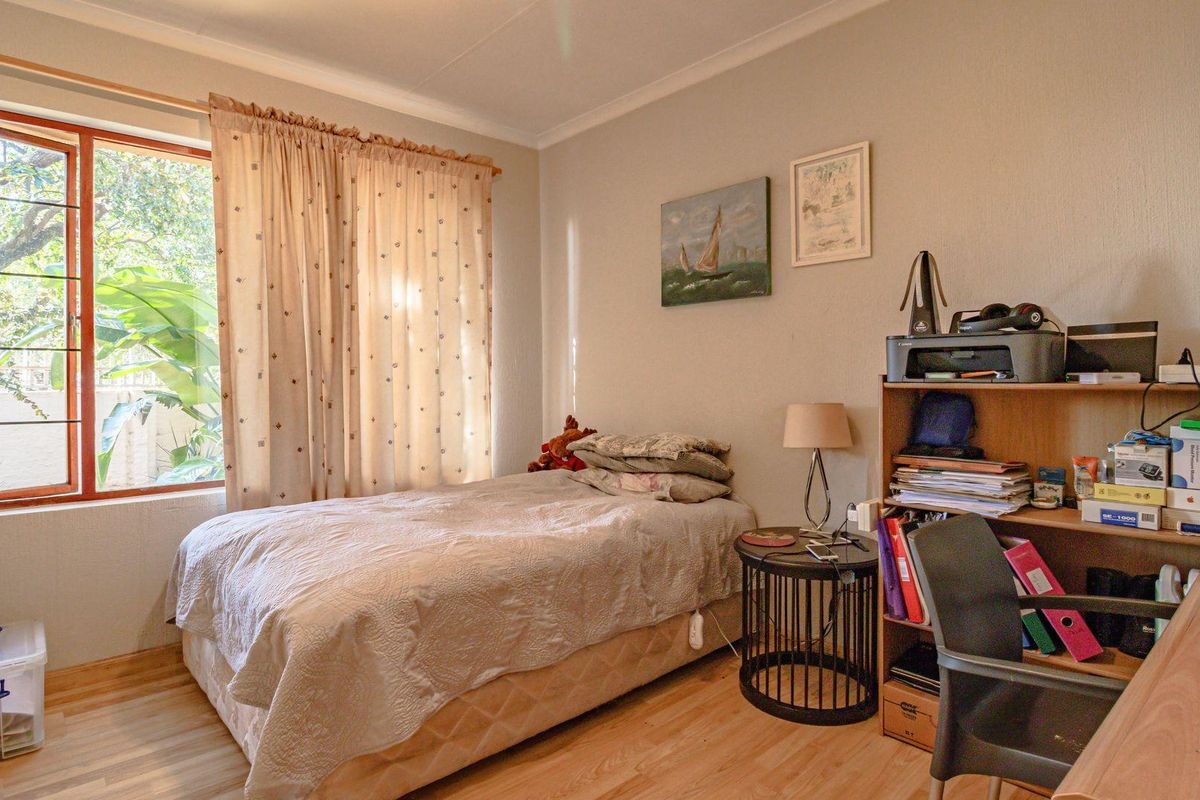 A well-lit bedroom featuring laminate flooring and a large window with garden views, providing a comfortable and functional living space.